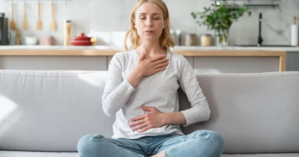Personne assise, mains sur le cœur et le ventre, en respiration apaisante, avec un verre d’eau à proximité
